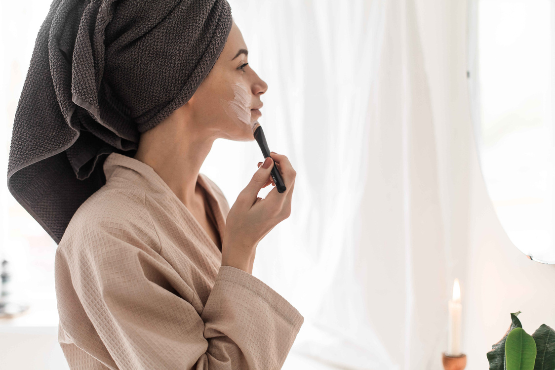 Woman in Bathrobe Applying Face Mask in Front of Mirror